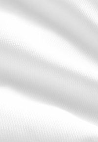 Gros plan d’un tissu blanc lisse avec une subtile texture diagonale et des reflets lumineux doux créant des ombres délicates.