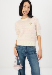 Kurzarmpullover in Creme mit rosa Streifen, verfügt über eine gestrickte Textur und eine dekorative Blumenbrosche. Kombiniert mit hochtaillierten Jeans.