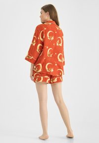 Röd pyjamasett med en tröja med trekvartsärmar och shorts, prydd med gyllene mån- och stjärnmönster. Tillverkad av mjukt tyg.