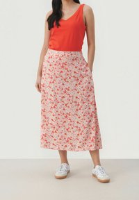 Haut sans manches rouge avec un décolleté en V associé à une jupe midi fluide ornée d'un motif floral pastel. La jupe a des poches latérales et est portée avec des baskets blanches.