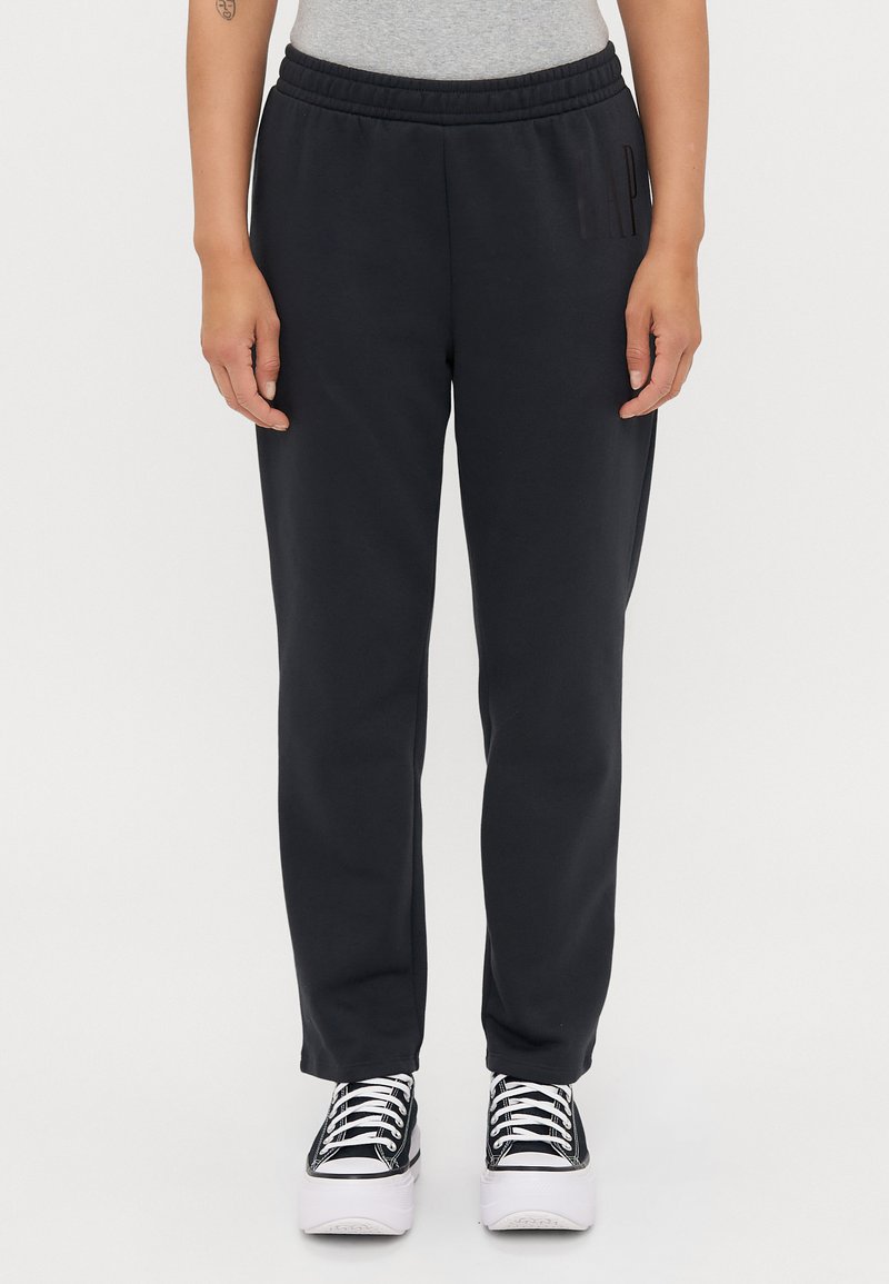 Pantaloni della tuta neri con vita elastica, caratterizzati da un dettaglio logo laterale. Abbinati a sneaker nere e bianche. Tessuto morbido e liscio.