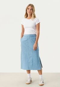 Modra jeans midi krila z navpičnimi belimi črtami, stranskimi razporki in žepi. Ujemajoče se s prilegajočo belo majico s kratkimi rokavi in športnimi copati.