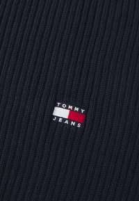 Námornícka rebrová tkanina s malou výšivkou loga, ktorá obsahuje červenú, bielu a modrú farbu a zobrazuje text "TOMMY JEANS".