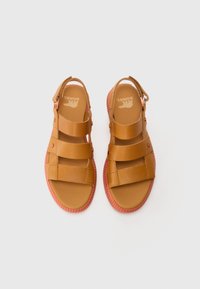 Brune lær sandaler med tre brede stropper og en rosa gummisåle. Justerbar ankelreim med metallspenne. Flat fotbed.