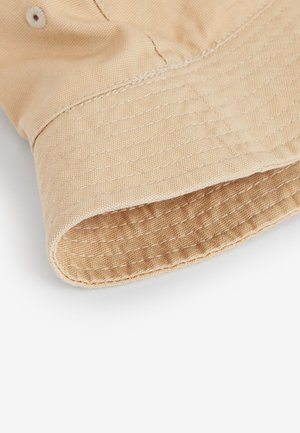 Bež platnena kapa kofa s teksturiranim uzorkom i vidljivim šavovima duž oboda, s podvrnutim rubom.