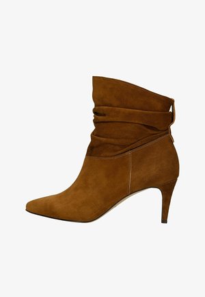 Stivaletto alla caviglia in camoscio marrone con tomaia morbida, punta a punta e tacco sottile di altezza media.