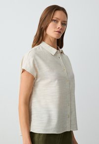 Blusa in lino beige chiaro a maniche corte con un davanti bottonato, colletto e una vestibilità comoda; tessuto leggero e lucentezza sottile.