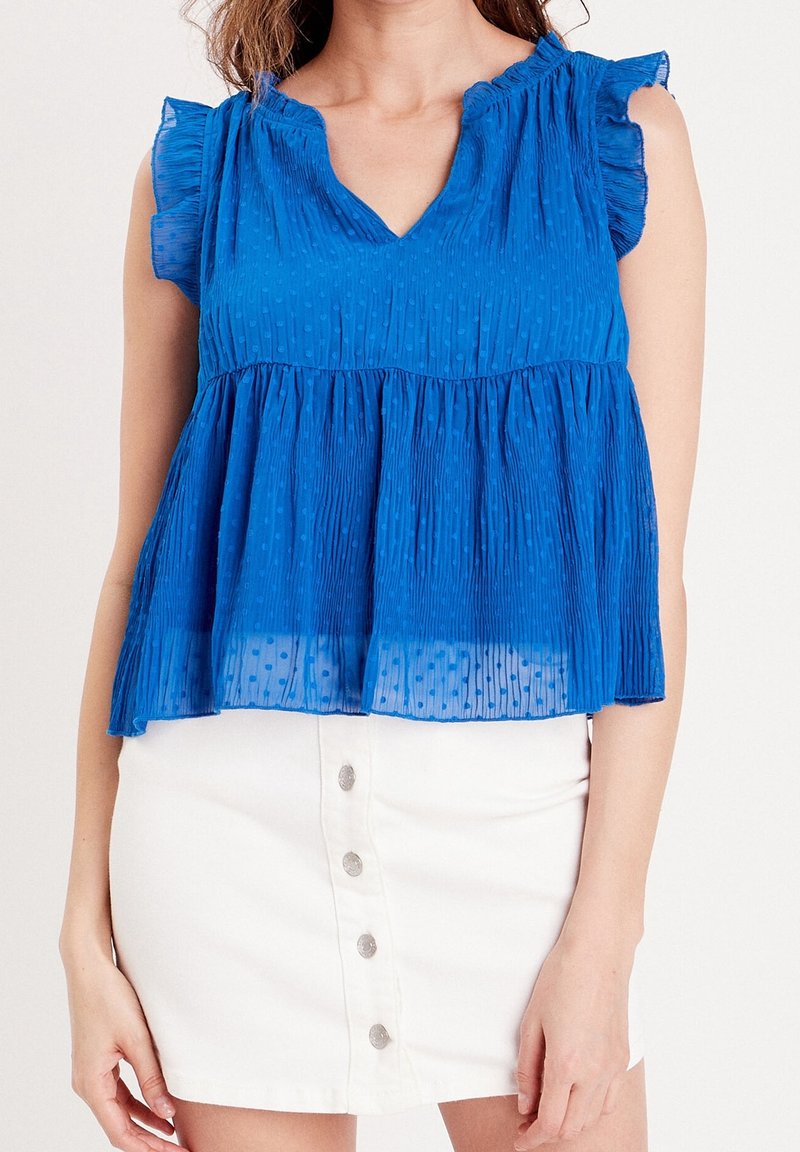 Haut bleu à manches courtes avec un col en V, des plis texturés et des manches à volants, associé à une jupe en denim blanche à boutons.