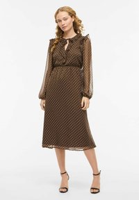 Brun polkadott midi-kjole med gjennomskinnelige ermer og volangkant ved halsen, knyttet i midjen. Kjolen har en glatt tekstur og flytende design.