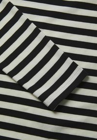 Tissu à rayures noires et blanches avec une texture douce. Les rayures sont uniformément espacées, avec un ourlet lisse au bord des manches.
