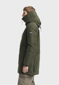 Parka verte et imperméable avec un col haut, une capuche ajustable, des poches avant et un patch logo sur la manche. Texture lisse et coupe ajustée.