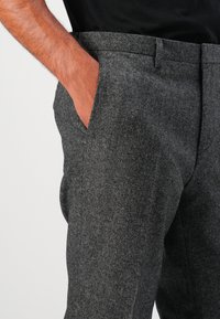 Grau gemischte Wollhose mit klassischem Design, seitlichen Taschen, flachem Vorderteil und taillierter Passform, die eine strukturierte Optik hervorhebt.