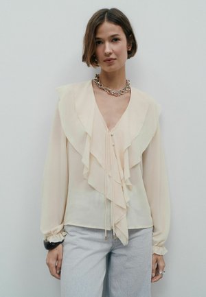 Helle cremefarbene Bluse mit Rüschen-Design auf der Vorderseite, langen Ärmeln und Knopfverschluss. Verfügt über eine zarte Textur und einen subtilen Glanz.