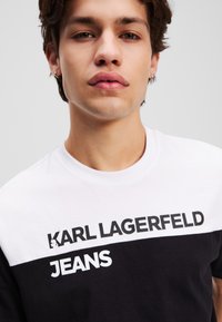 Juoda ir balta medvilninė marškinėliai su spalvų blokų dizainu, išryškintu spaudu "KARL LAGERFELD JEANS" priekyje.