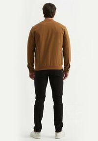 Veste en cuir marron avec une texture lisse, poignets et ourlet côtelés, associée à un pantalon slim noir et des baskets blanches. Vue de dos.