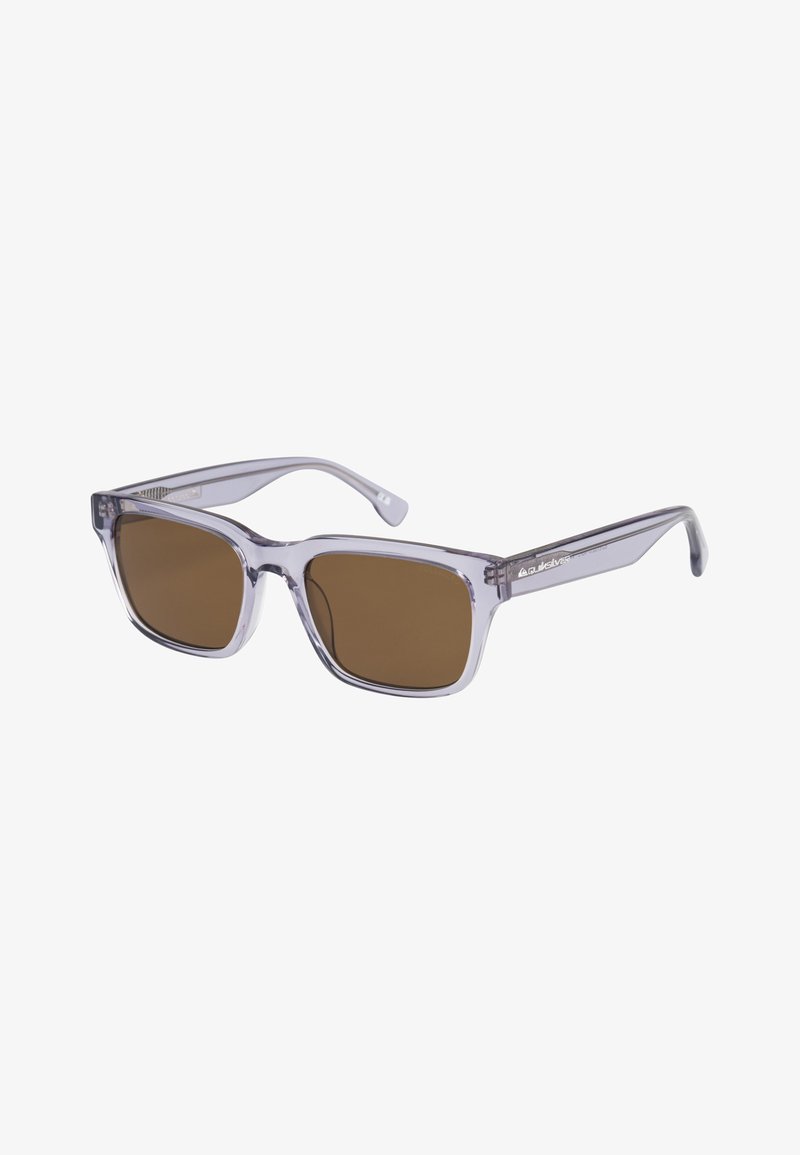 Przezroczyste plastikowe okulary przeciwsłoneczne z kwadratowymi oprawkami, brązowymi soczewkami oraz eleganckimi, zaokrąglonymi ramionami. Charakteryzują się minimalnym oznakowaniem po boku.