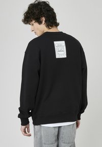 Sweatshirt noir à manches longues et à coupe décontractée. Présente un graphique blanc d'un magasin de disques au dos, fabriqué dans un tissu doux.