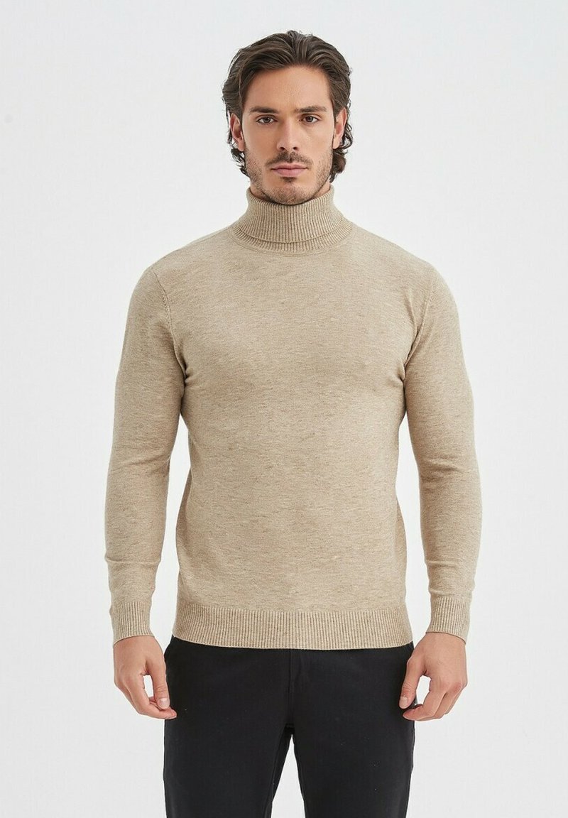 Un pull à col roulé beige avec des manches longues, des poignets et un ourlet côtelés. Texture douce avec un design ajusté, porté sur un pantalon noir.