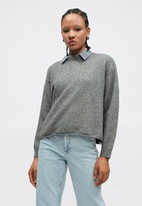Gray knitted sweater with a blue and white striped collar, relaxed fit, long sleeves, and side slits, worn with light wash jeans.