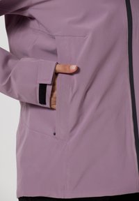 Giacca di un delicato viola chiaro con chiusura a zip, polsini regolabili e tasca laterale. Il tessuto ha una finitura liscia e testurizzata.