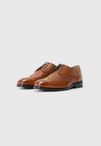 Zapatos de vestir de cuero marrón con un acabado suave y detalles perforados en los laterales; diseño clásico de cordones, con tacón bajo.
