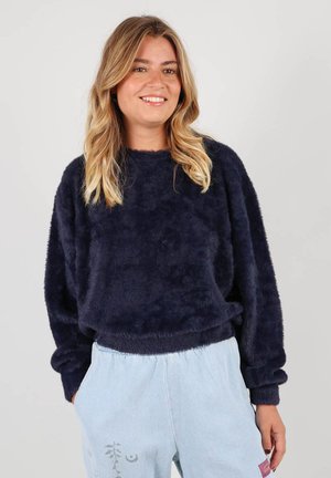 Un sweat à col rond en bleu marine, doux, à manches longues et à la coupe décontractée, associé à un pantalon bleu clair avec un motif sur une jambe.