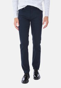 Pantaloni in cotone blu navy con vestibilità slim, design a cinque tasche, texture sottile, abbinati a scarpe eleganti nere lucide.