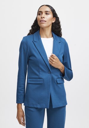 Modrý přizpůsobený blazer s klopovým límcem, jedním zapínáním na knoflík, dvěma předními kapsami a hladkou texturou, doplněný bílým topem.