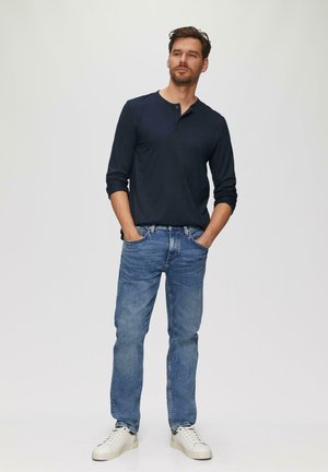 Marineblaues Langarm-Henley-Shirt, blaue Jeans und weiße Sneakers. Slim Fit, lässiger Stil, mit Rundhalsausschnitt und minimaler Ausstattung.