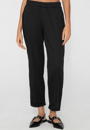 Černé kalhoty s elastickým pasem a ohrnutými lemy, nošené s černými špičatými botami Mary Jane se stříbrnými očky.