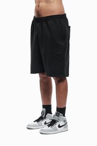 Fekete rövidnadrág elasztikus derékpánttal, oldalzsebekkel és tónusú logó hímzéssel. Szürke és fekete magas szárú sportcipővel párosítva.