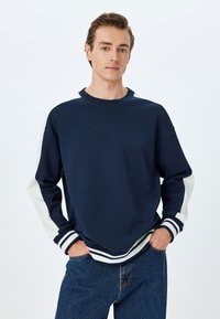 Mörkblå sweatshirt med vita panelaccent på ärmar, ribbade mudd och nederkant, tillverkad av ett mjukt tyg, med en rundad halsringning.
