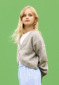 Grå ullcardigan med V-hals och långa ärmar, tillsammans med ljusblå randiga byxor. Enhetlig grön bakgrund.