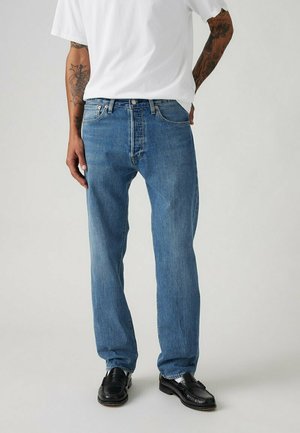 Jeans in denim blu chiaro con una vestibilità morbida, caratterizzati da un classico design a cinque tasche e dettagli cuciti, abbinati a una t-shirt bianca e mocassini neri.