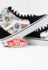 Černé květinové vysoké tenisky s bílými tkaničkami a gumovými podrážkami, na bílém pozadí s červenou cedulkou "Vans Off the Wall".