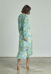 Lungo vestito fluido con un motivo acquerello blu e verde, caratterizzato da scollatura e maniche arricciate, orlo svasato e vita elastica.