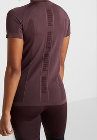 Viininpunainen urheilupaita teksturoidulla kuviolla, lyhyet hihat ja pystysuuntainen PUMA-logo selän keskellä, yhdistetty samansävyisiin shortseihin.