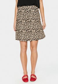 Leopardenmuster-Rock in Beige und Schwarz, ausgestellter Schnitt, knielang. Glatte Textur aus leichtem Material. Tragend mit roten Ballerinas.