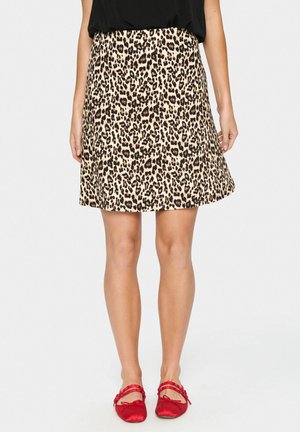 Jupe imprimé léopard beige et noir, design évasé, longueur genou. Texture lisse avec un matériau léger. Portée avec des ballerines rouges.