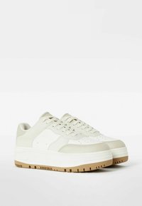 Tenisky s bílým a krémovým koženým svrškem, texturovanými akcenty a silnou gumovou podrážkou s béžovým vzorem.