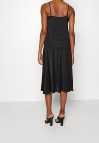 Svart satin klänning med spagettistropper, en åtsittande överdel och en flödande plisserad kjol. Inkluderar svarta sandaler med klossklack.