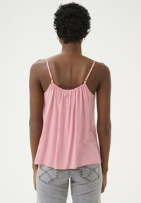 Roza brezrokavnik s nabranim hrbtom, z nastavljivimi naramnicami in sproščenim krojem, v kombinaciji z svetlo sivo denim hlačami.