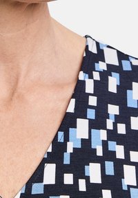 Marintopp med V-ringning och ett geometriskt mönster av rektanglar i olika storlekar och nyanser av ljusblått och vitt. Slät textur.