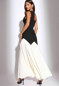 Rochie de seară neagră și crem, cu un corset ajustat și fustă evazată, având accente transparente negre la umeri și o linie a tivului diagonală.