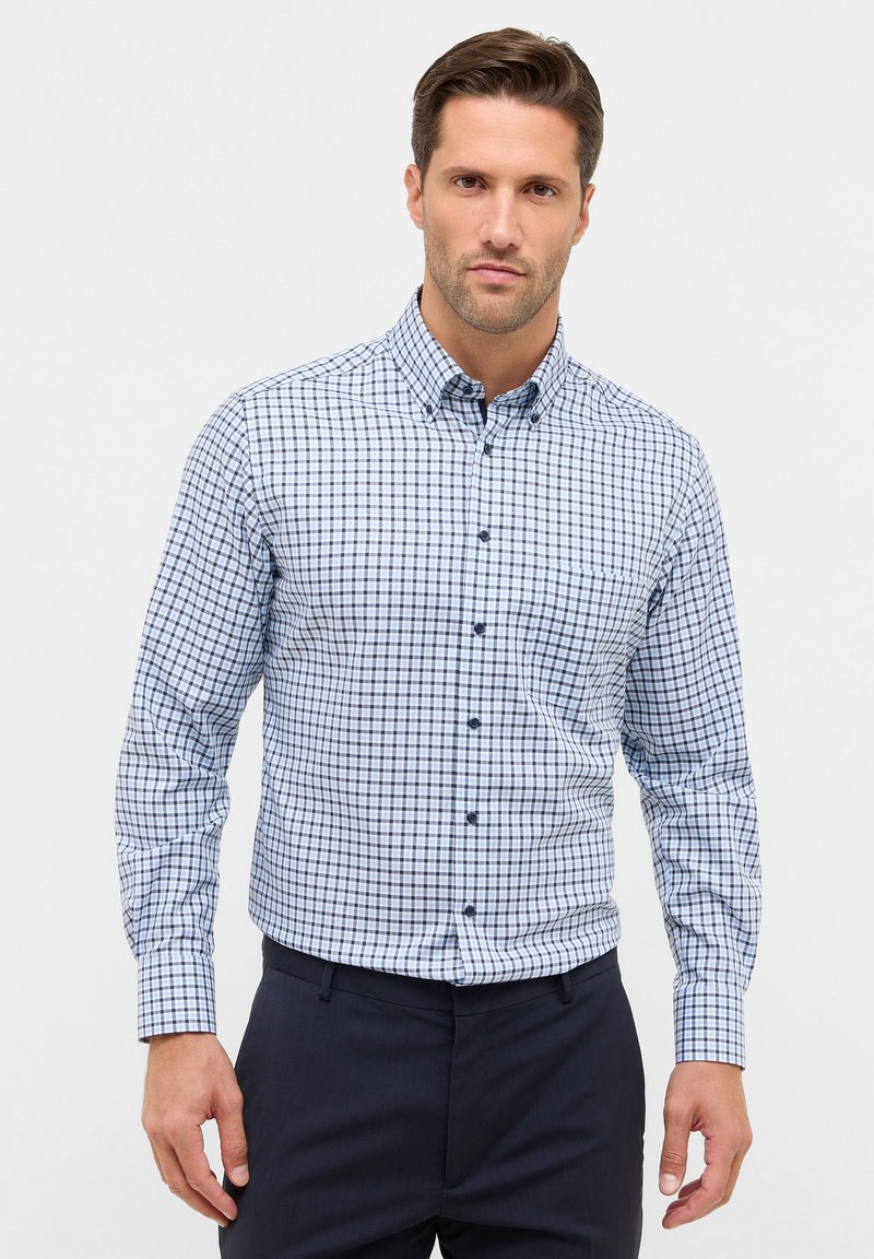 Gecarodeerde button-up blouse in wit, blauw en marineblauw. Heeft een kraag, lange mouwen en een enkele borstzak met blauwe knopen.