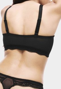 Black bralette with adjustable straps, lace trim, and seamless design. Smooth fabric and minimal hardware for comfort and subtle elegance.