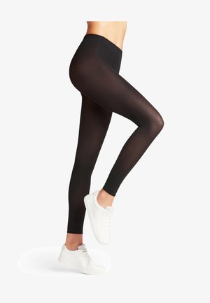 Leggings noirs avec une taille haute, une texture lisse et un design ajusté, associés à des baskets basses blanches.