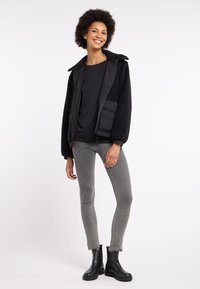 Zwarte fleecejas met een ritssluiting, kraag en een voorkauw. Draagt over een zwart top en gecombineerd met grijze slim-fit jeans en zwarte laarzen.