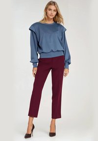 Niebieska bluza z oversize'owymi rękawami, w połączeniu z bordowymi spodniami o dopasowanym kroju. Gładka tekstura materiału, dopasowana talia i klasyczny dekolt.