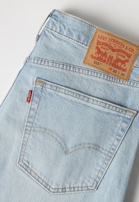 Ανοιχτά μπλε τζιν Levi's που δείχνουν την πίσω τσέπη με κόκκινη ετικέτα Levi's και καφέ δερμάτινο σημάδι бренτης με λεπτομέρειες μεγέθους και μοντέλου.